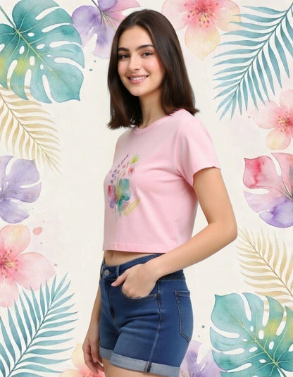 Woman wearing a pink floral crop top and blue shorts against a colorful leaf and flower patterned background.