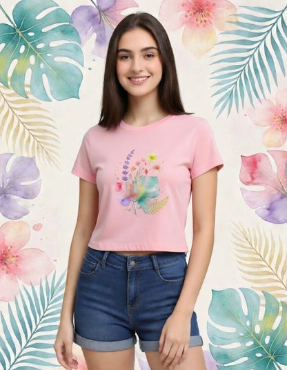 Woman wearing a pink t-shirt with a colorful design and blue shorts against a floral and leaf patterned background.